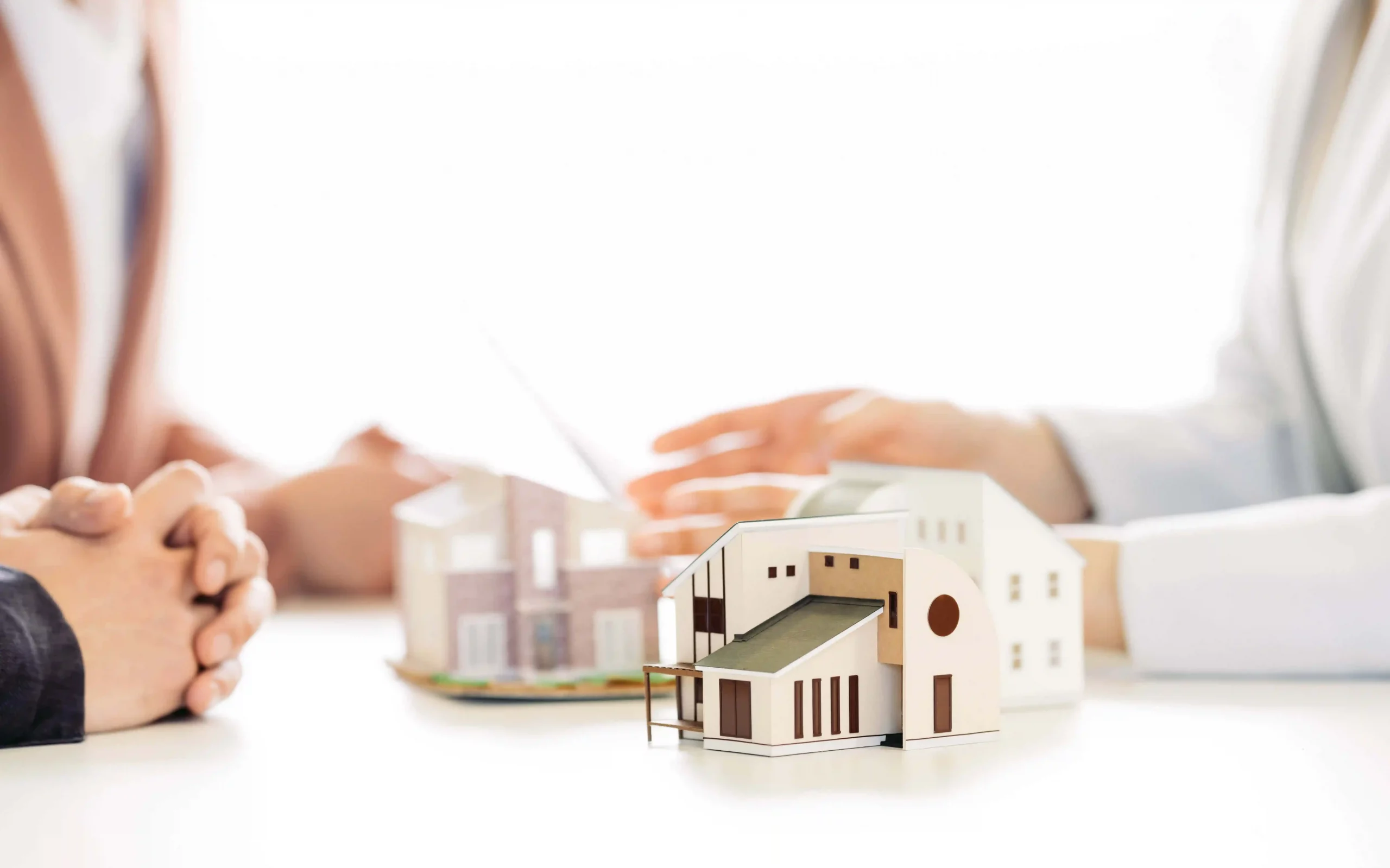 Architekturmodell auf Tisch bei Immobilienberatung mit Händen im Hintergrund
